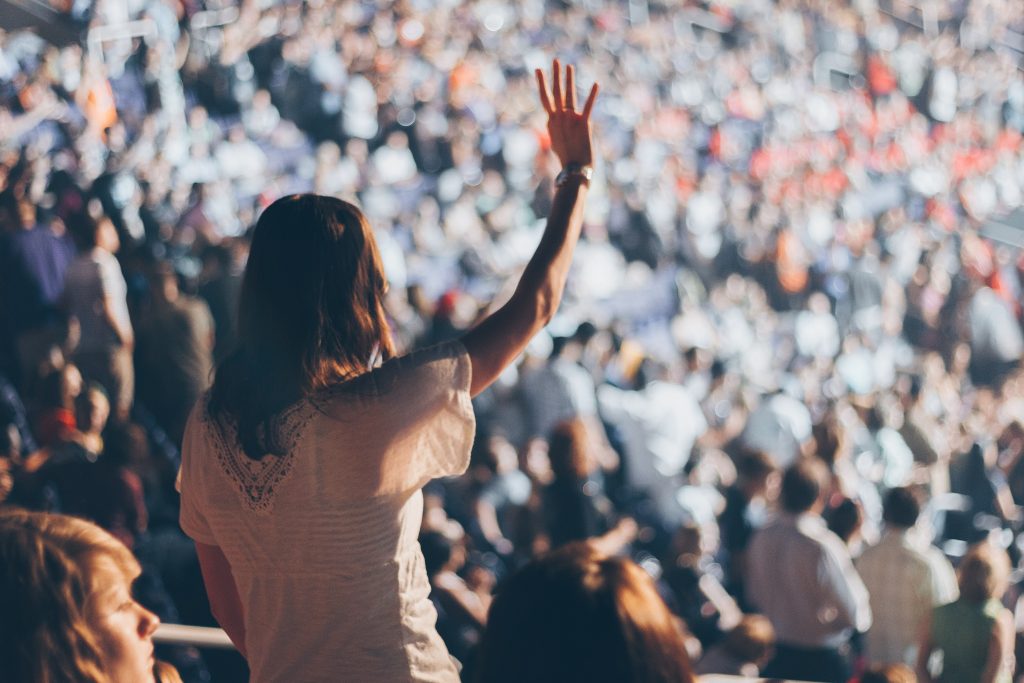 Woman standing up raising hand in large audience crowd